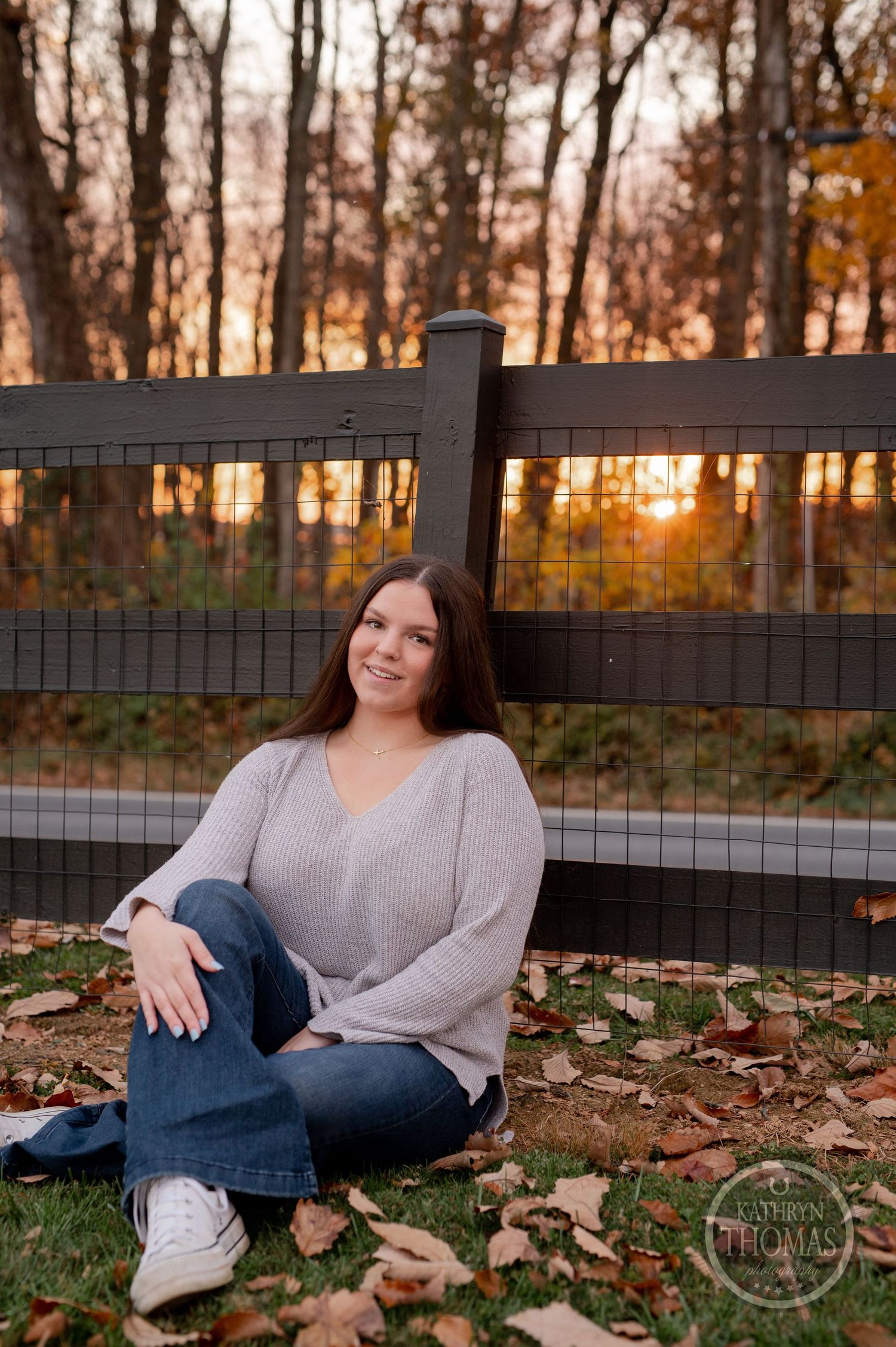 Casual portrait by wooden fence at sunset with fall foliage.