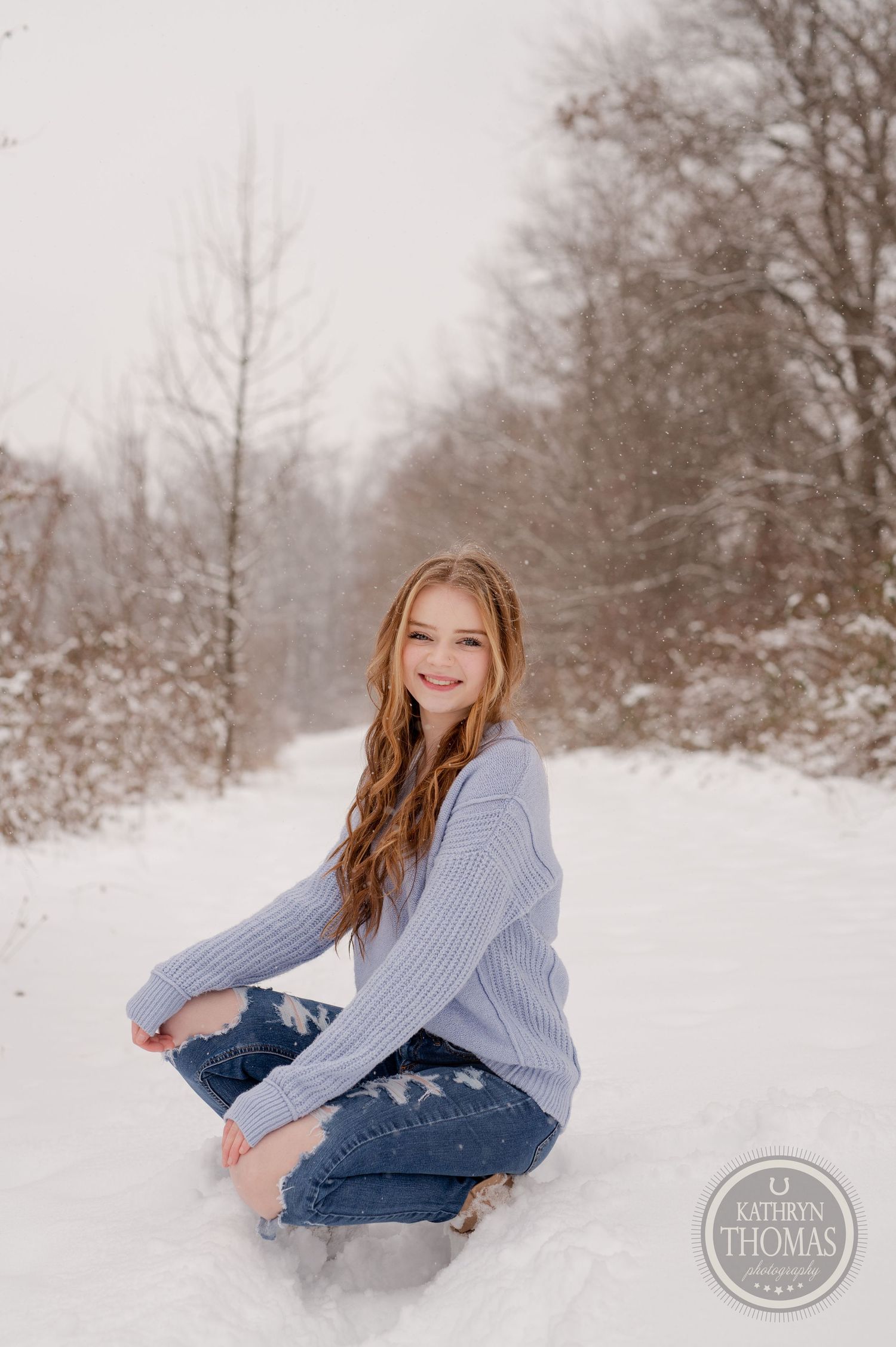 Winter portrait session in the snow featuring casual style with ripped jeans and a cozy sweater.