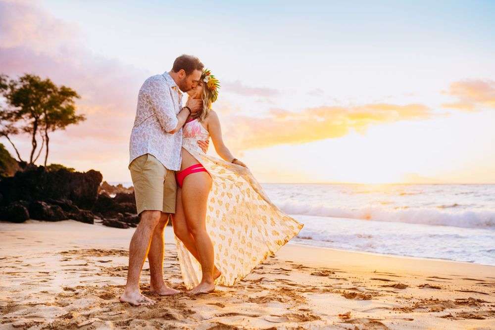 sunrise maternity photos in wailea. Couple enjoying romantic moment on sandy beach during vibrant sunset.