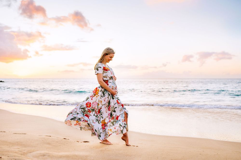 makena maternity photography beach. Sunset beach maternity photoshoot with floral dress and flowing fabric creating romantic silhouettes.