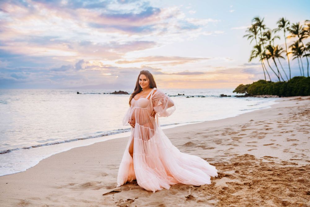 luxury maternity photography for women on maui. Person in flowing pink dress walking along sandy beach at sunset with palm trees.