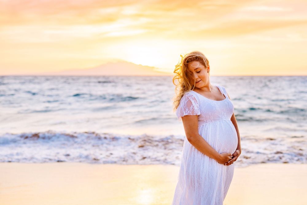 sunset wailea babymoon photography. Person in white dress walking along beach during golden sunset with waves.