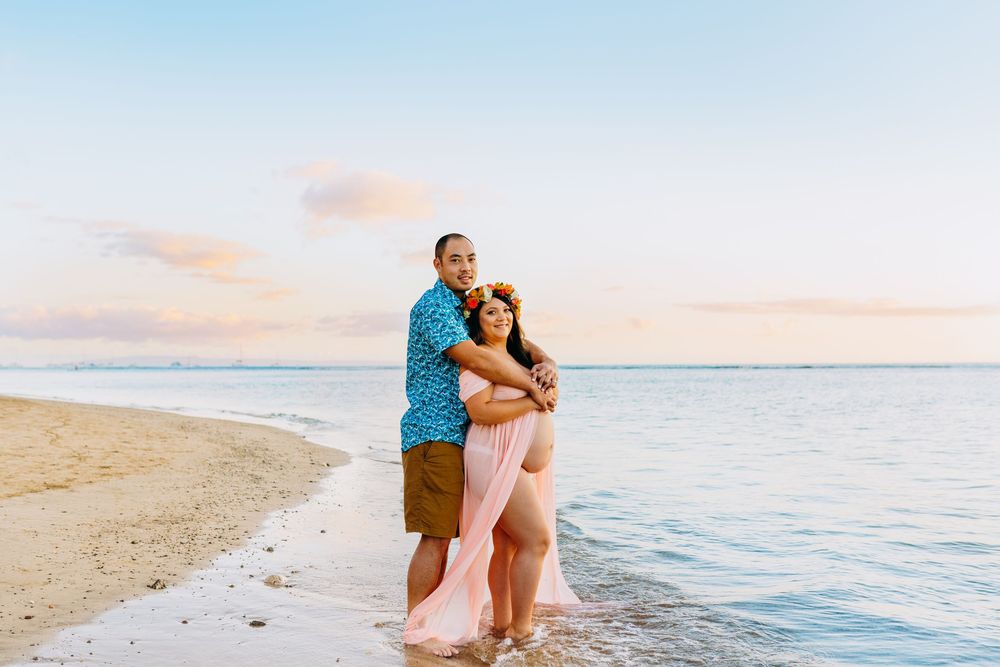 lahaina maternity photography. Romantic beach maternity session with couple embracing on sandy shore at golden hour.