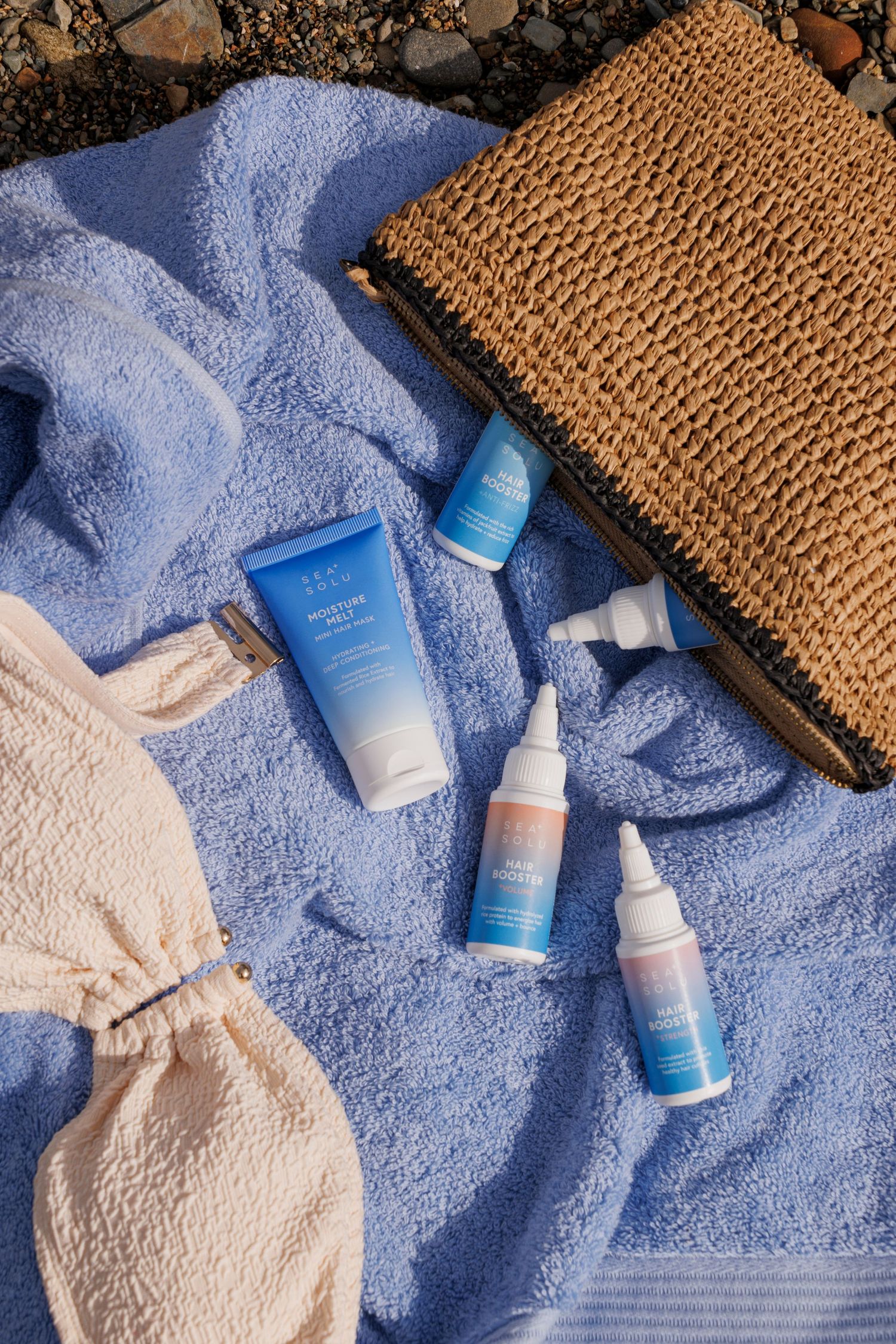 Blue skincare products displayed on beach towel with straw bag and accessories.