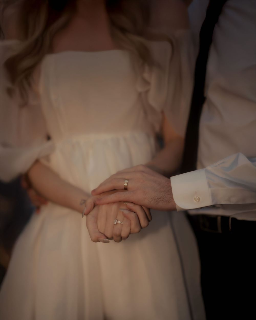 Close-up of clasped hands showing wedding rings against a white dress.