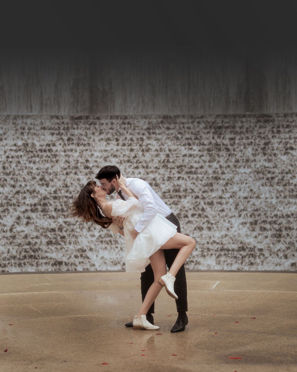 Dramatic dance dip pose against a rustic brick wall background.