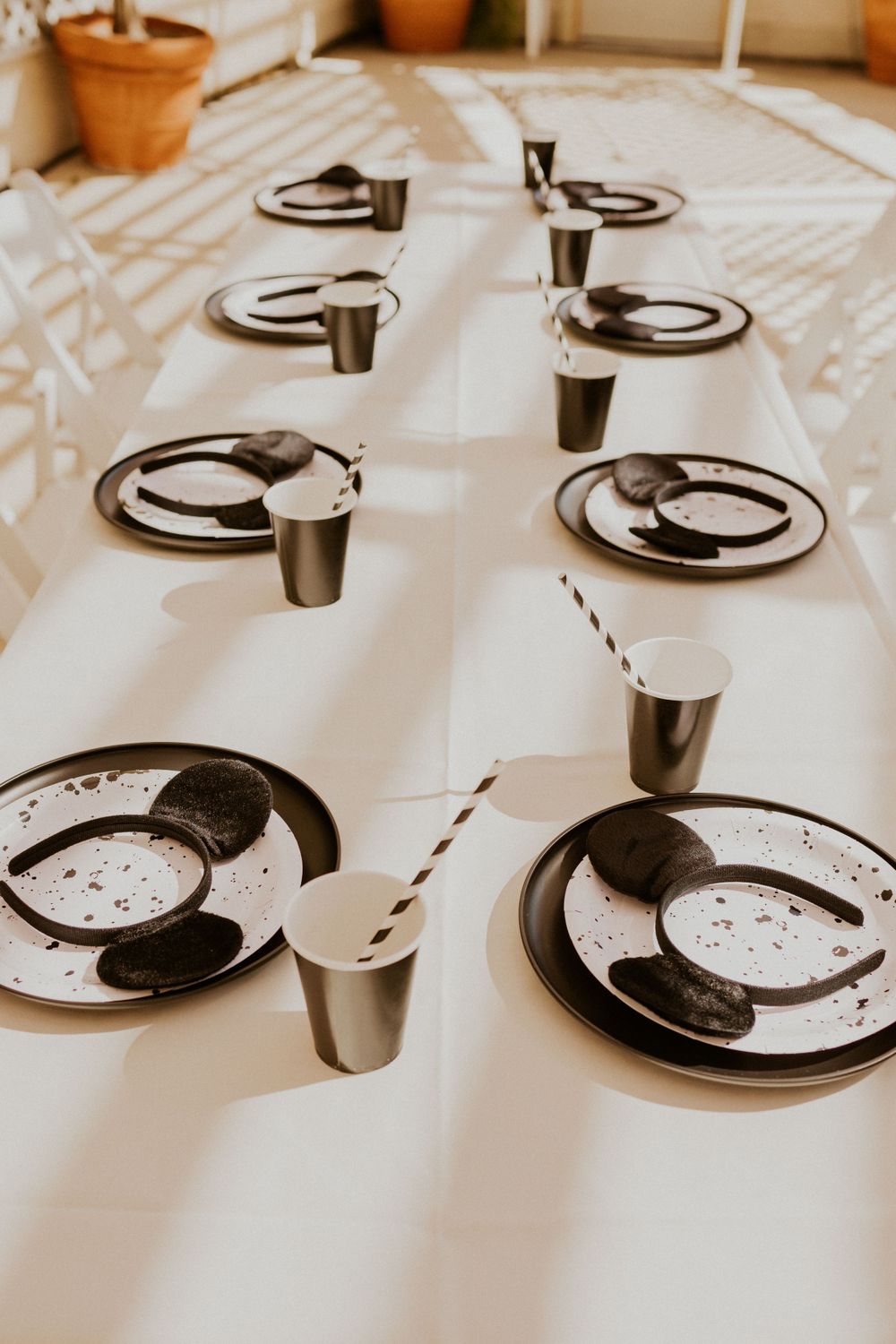 Black and white place settings with striped straws arranged on a long white tablecloth.