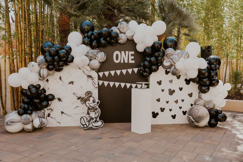 Elegant black and white balloon arch with Mickey Mouse silhouettes and 'ONE' signage for a first birthday celebration.