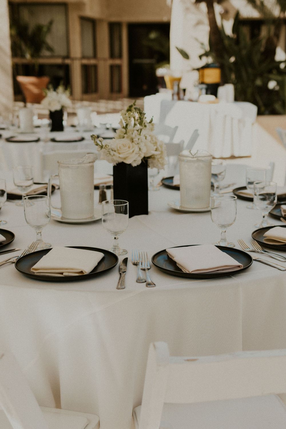 Formal dining table setup with white linens, black charger plates, and floral centerpieces.