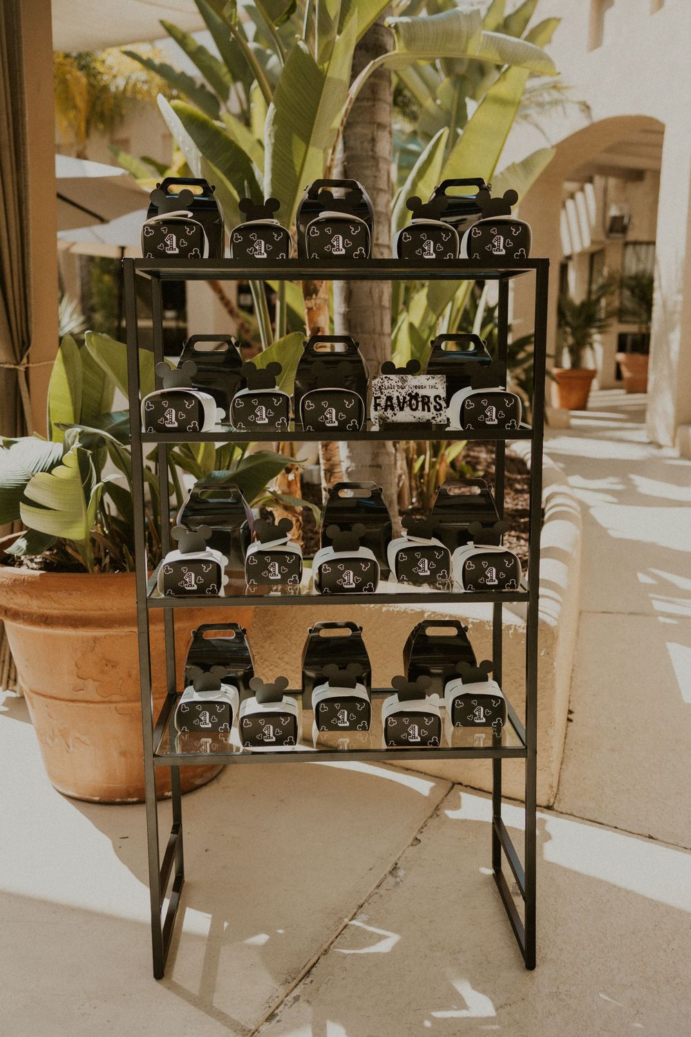 Display rack of black Mickey Mouse themed party favors with tropical plant backdrop.