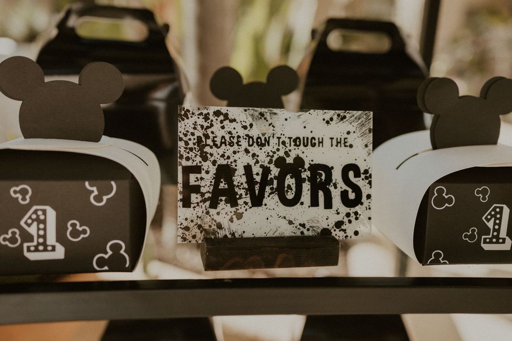 Black Mickey Mouse themed party favor boxes with hearts and number one design on display at a birthday party.