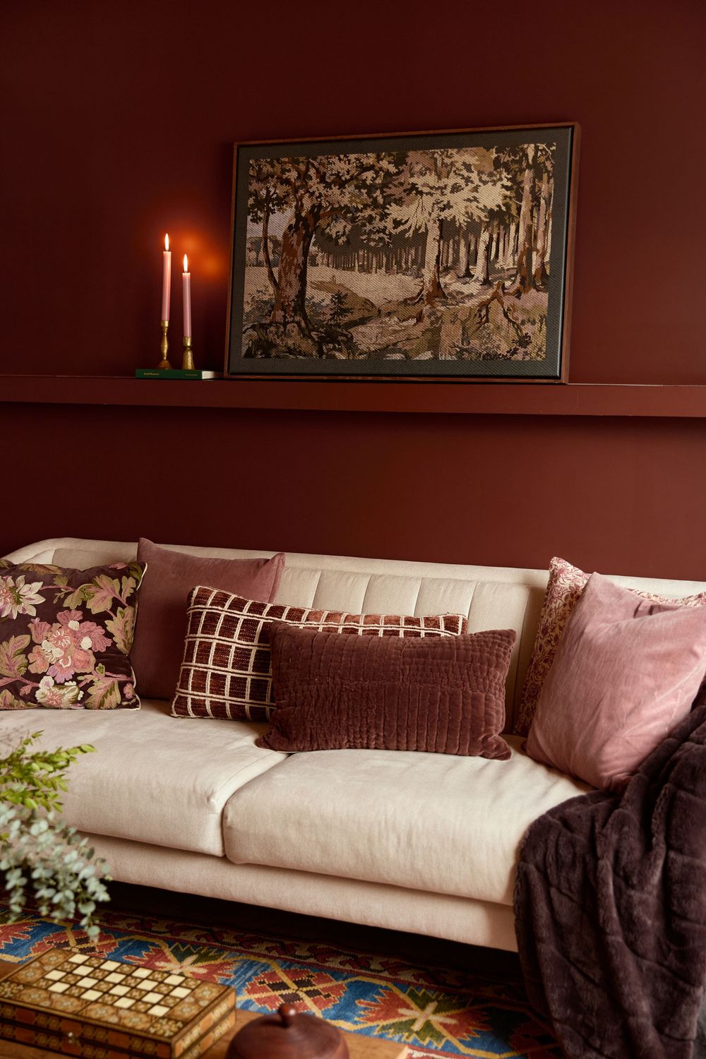 A cozy living room setting with a white sofa, burgundy walls, and decorative artwork features soft lighting and textured pillows.