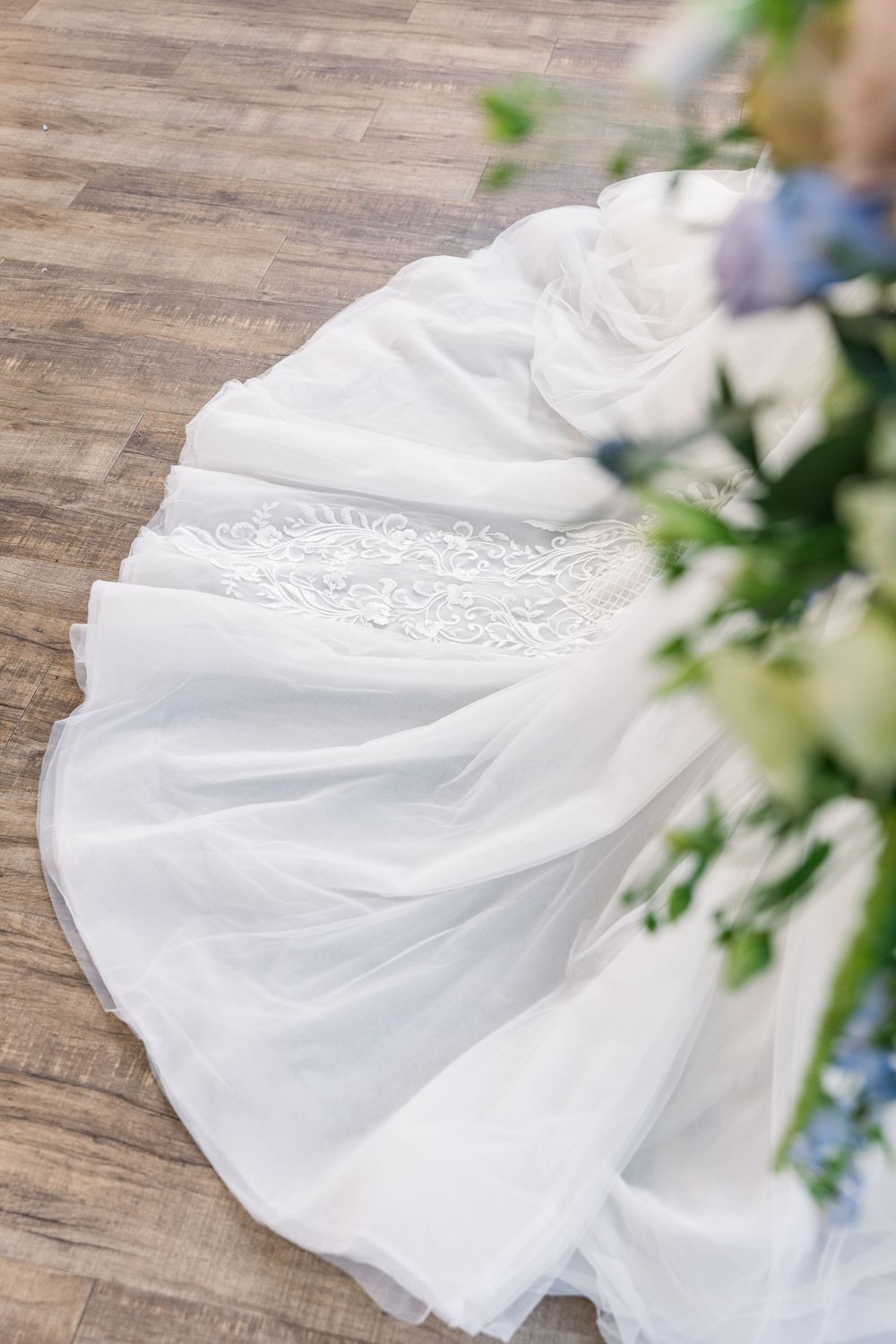 Close-up detail of intricate white wedding dress train on wooden floor.