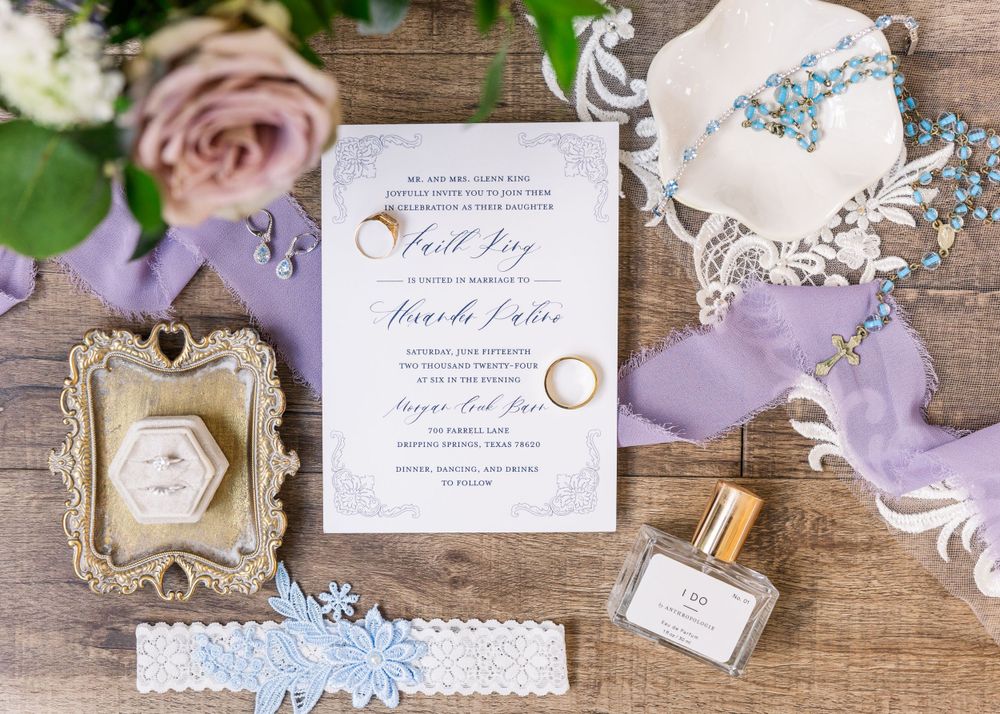 Wedding invitation suite with purple accents, rings, and delicate accessories on wooden surface.