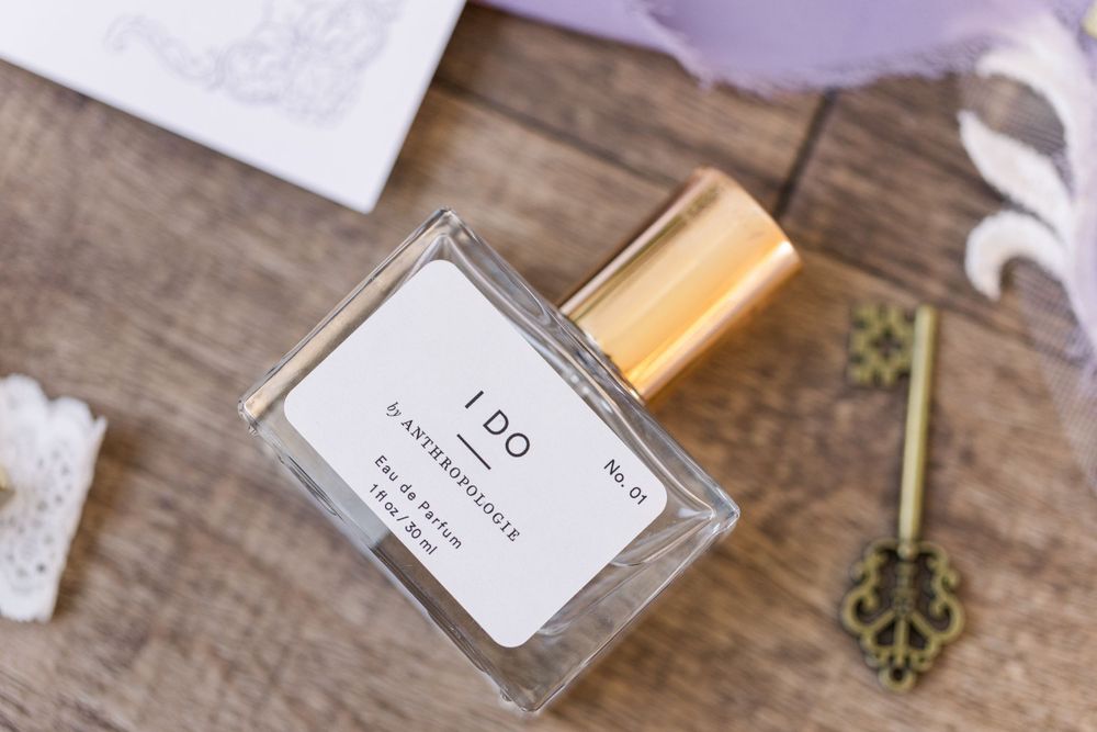 Glass perfume bottle with gold cap and label displayed on rustic wooden surface with vintage key.