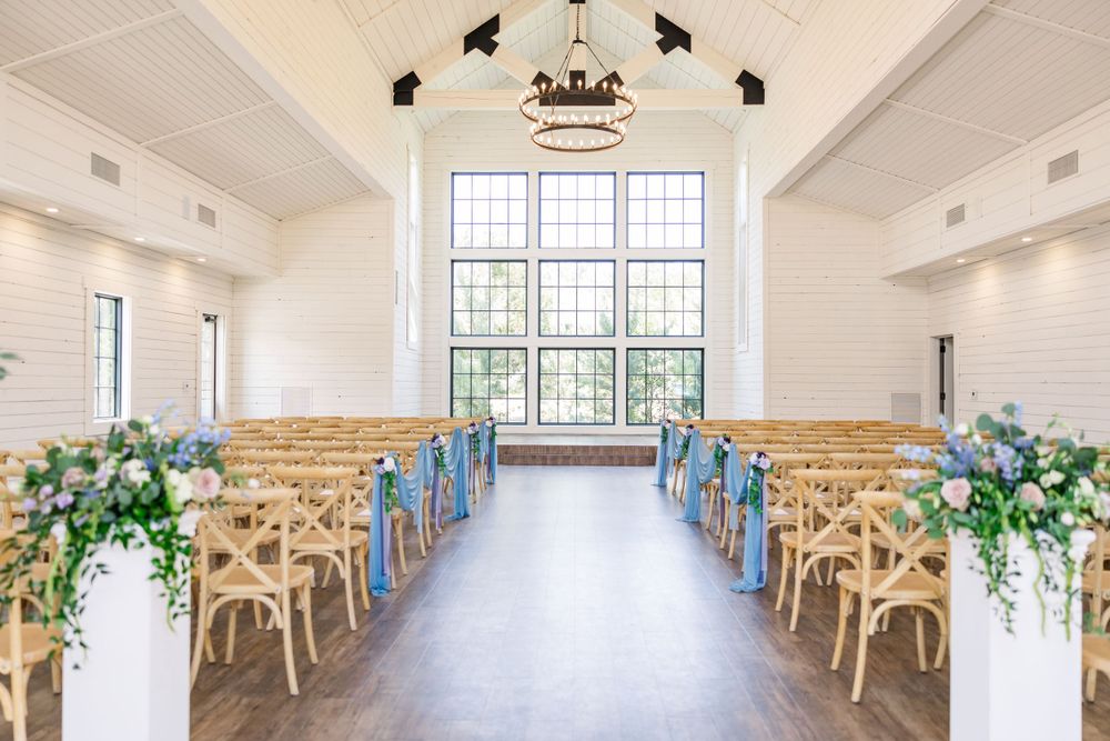 Light-filled wedding chapel with wooden cross-back chairs and floral arrangements lining the aisle.