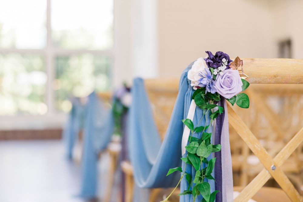 Decorative blue ribbons and purple flowers adorn wooden ceremony chairs.