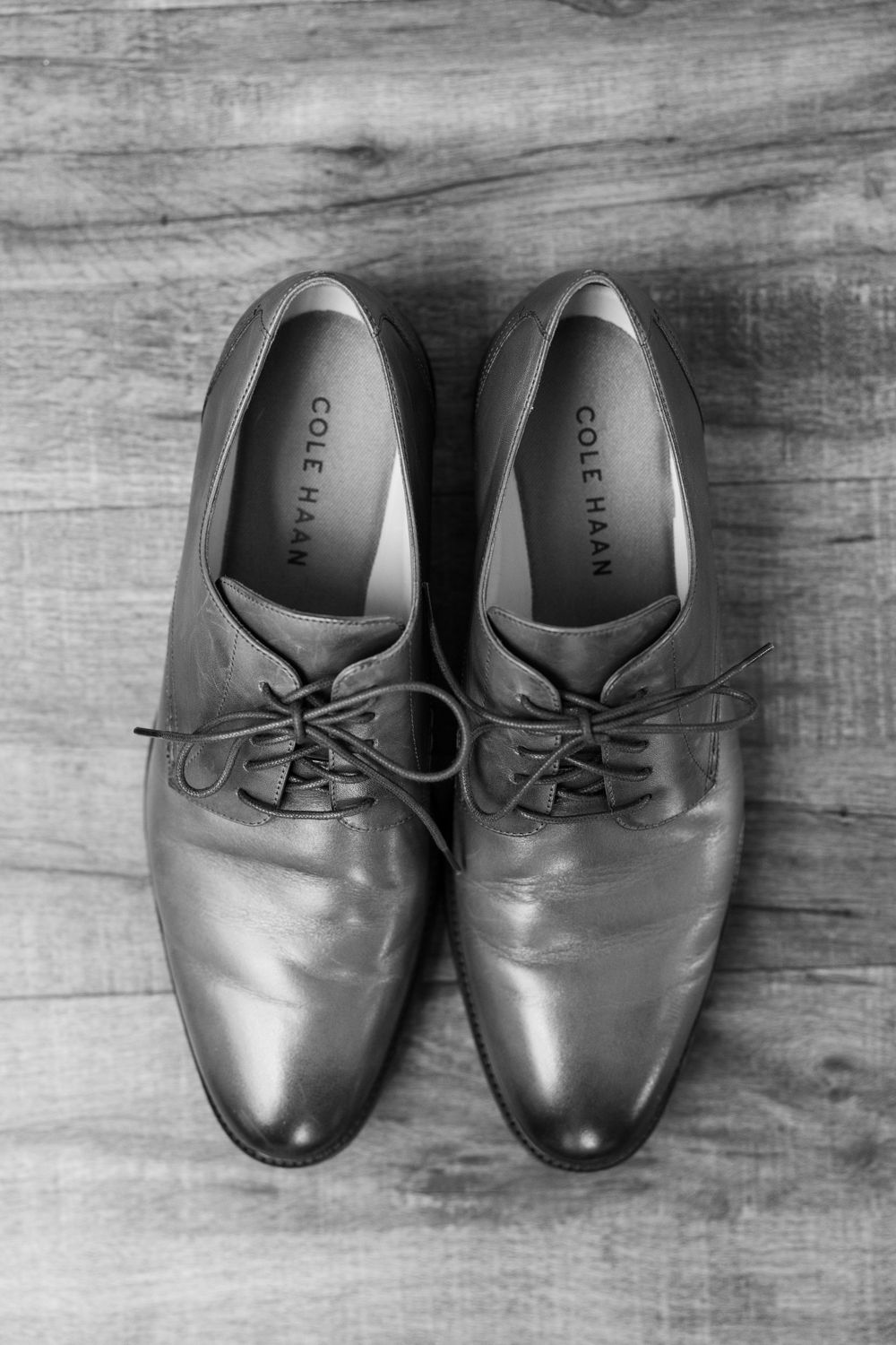 A pair of polished grey leather dress shoes on a wooden surface, shot in black and white.