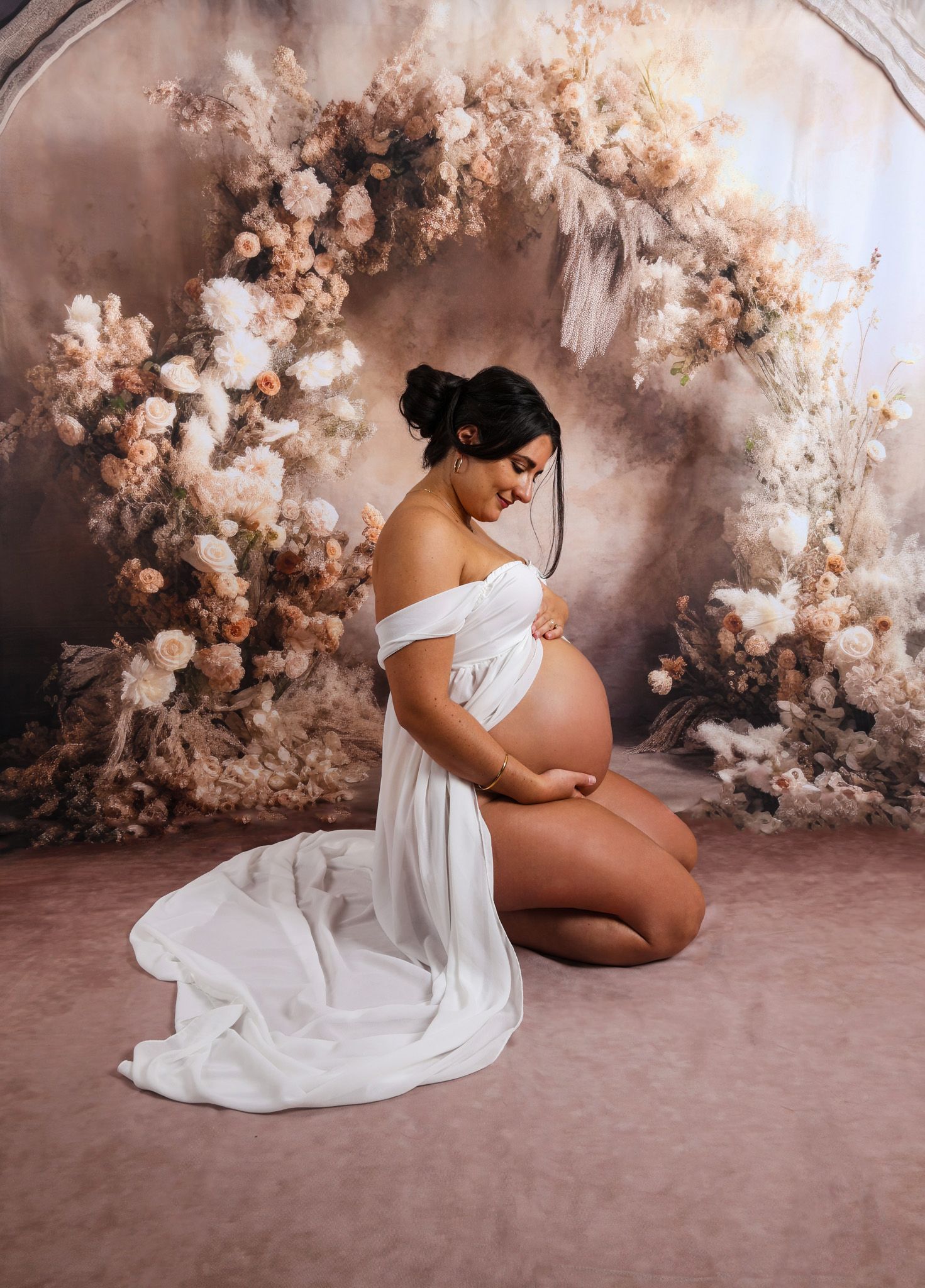Elegant maternity session featuring white dress against romantic floral backdrop.