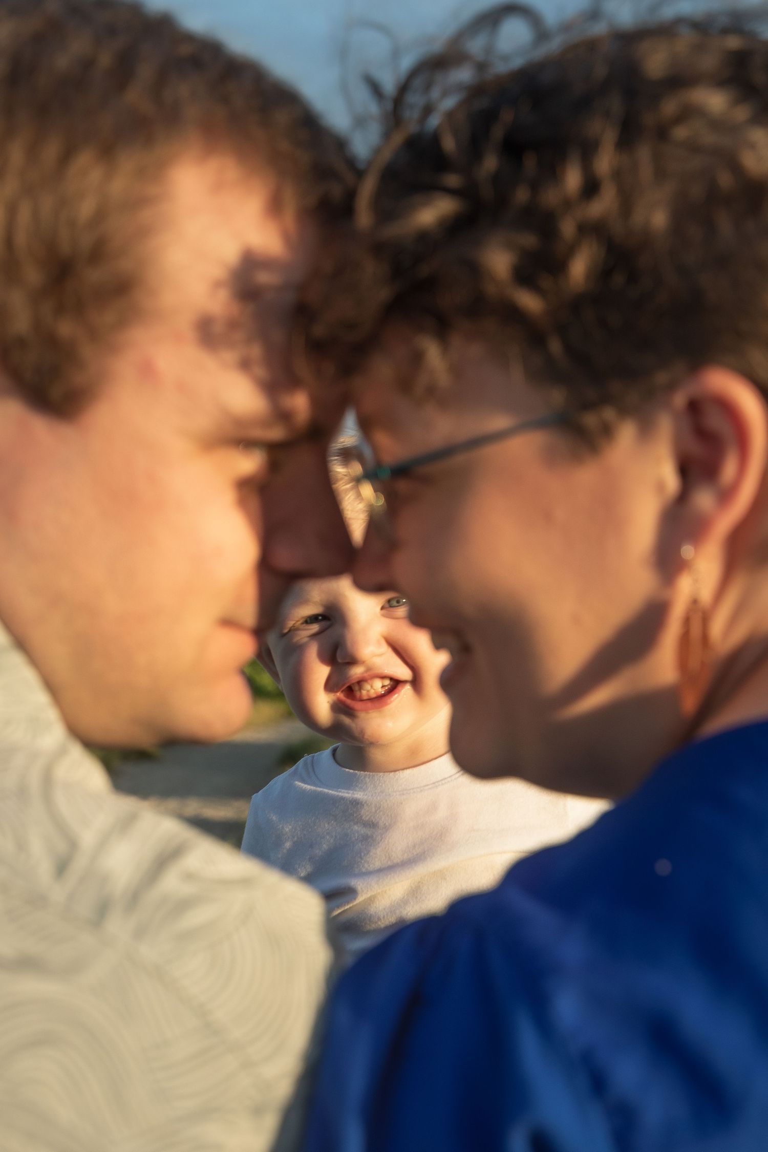 A joyful child smiles between two adults in an intimate family portrait with warm lighting and soft focus.
