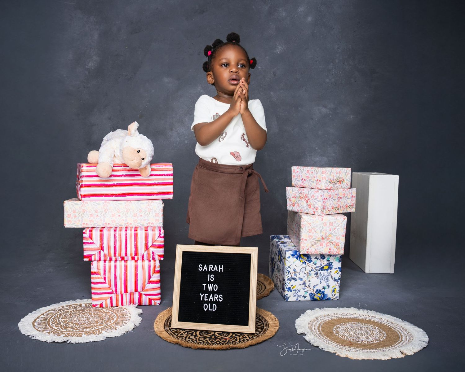 A young girl named Sarah celebrates her 2nd birthday surrounded by colorful gift boxes and a letter board sign.