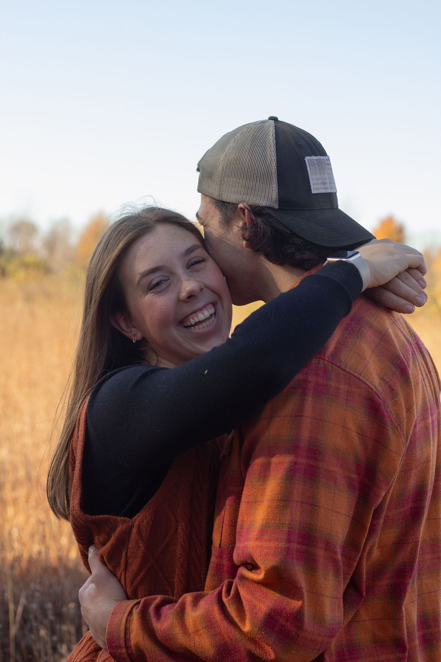 A couple embraces in a field during golden hour as sunlight illuminates the autumn grass behind them during autumn couples photos.