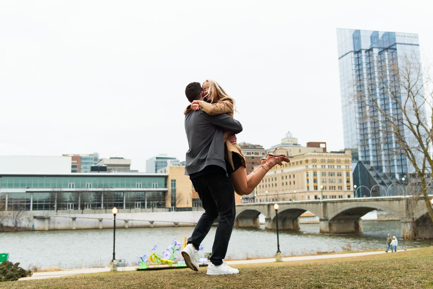 A couple embraces and spins joyfully along the Grand River and city buildings in the background.