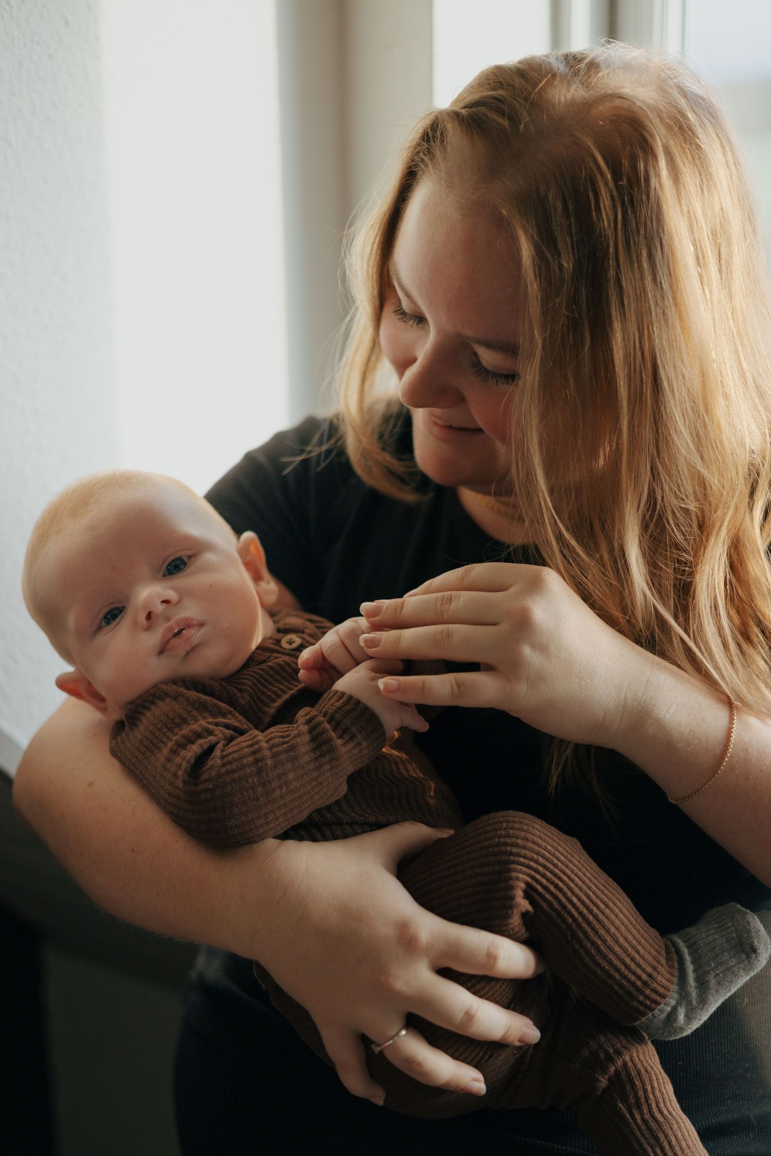Intimate portrait of parent and baby sharing gentle moment by window.