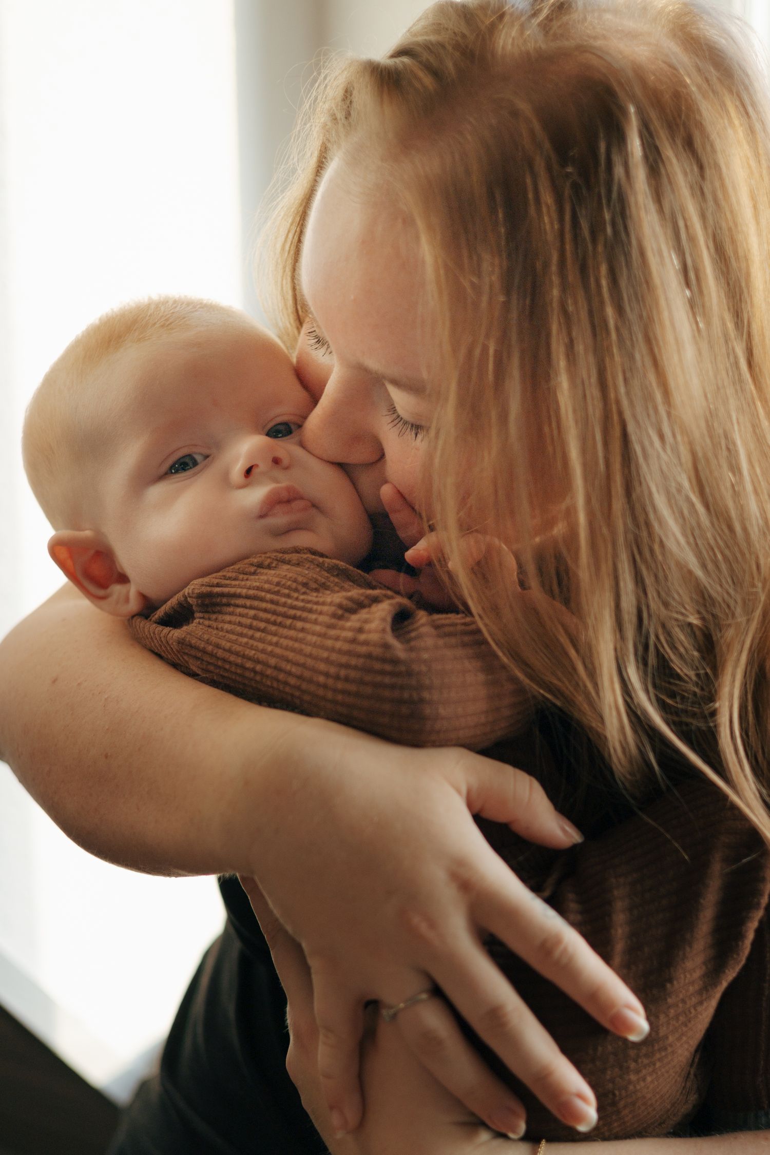 Sweet bonding moment between parent and infant in brown sweater by window.