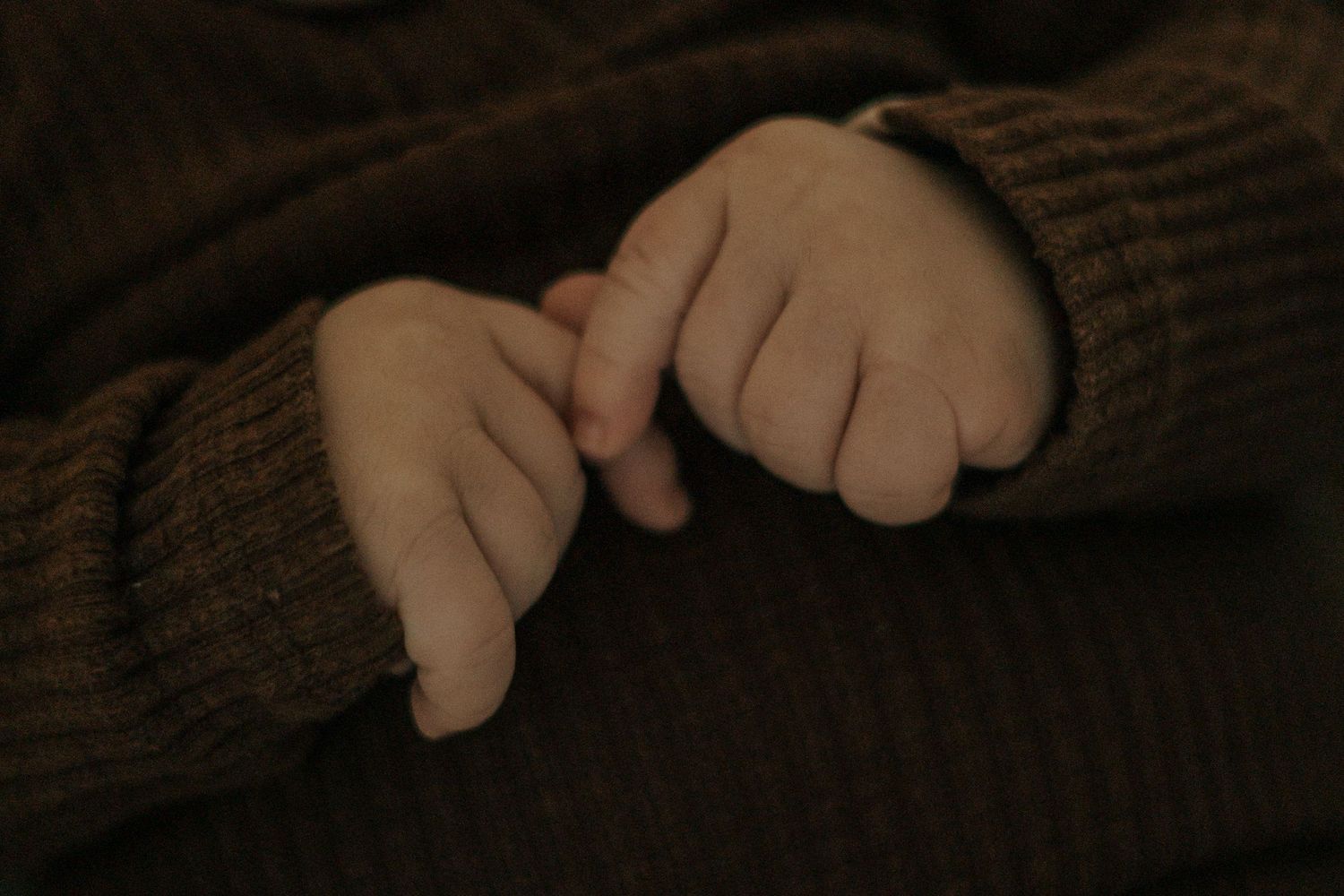 Close-up shot of tiny hands grasping in warm brown tones.