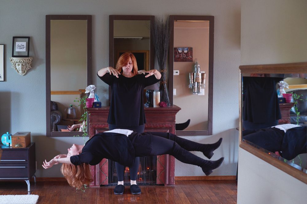 Person performing a playful jumping pose in a living room with furniture and mirrors.