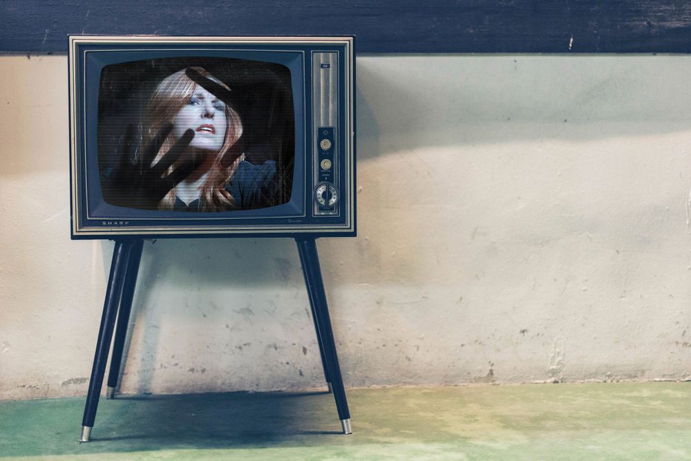 A vintage television set on legs displays an artistic black and white portrait against a textured wall.