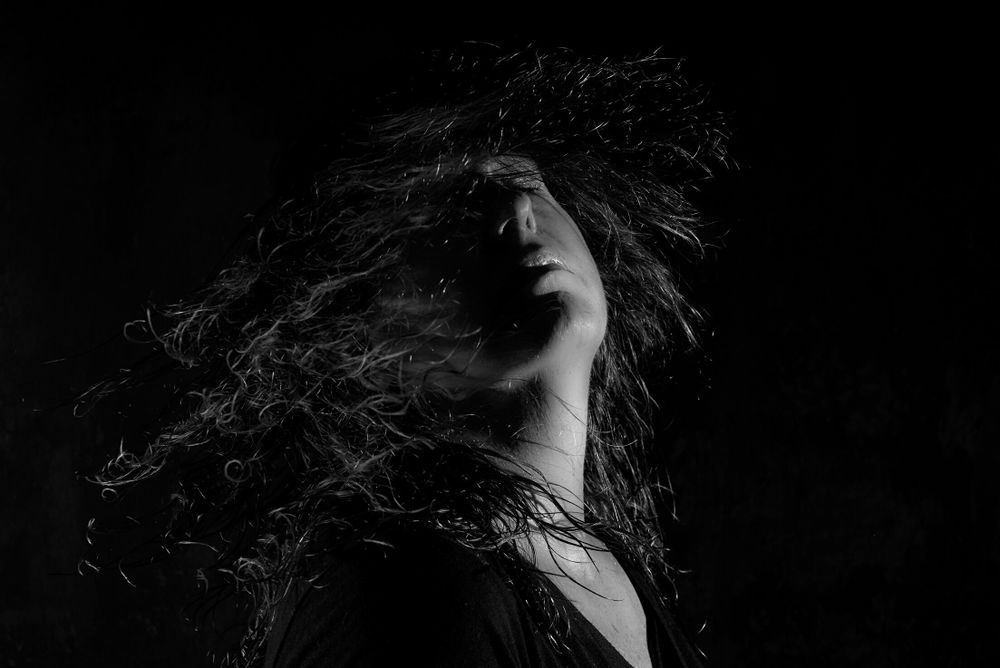 Dramatic black and white portrait showing silhouetted figure with windswept hair against dark background.
