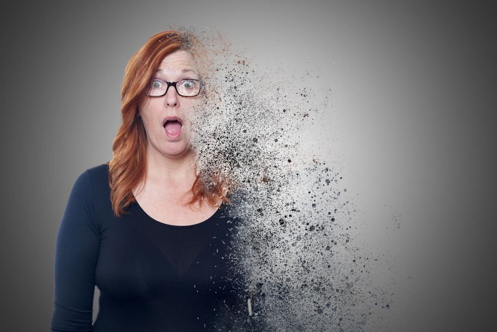 Creative portrait showing a figure in black dissolving into particles against a gray background.