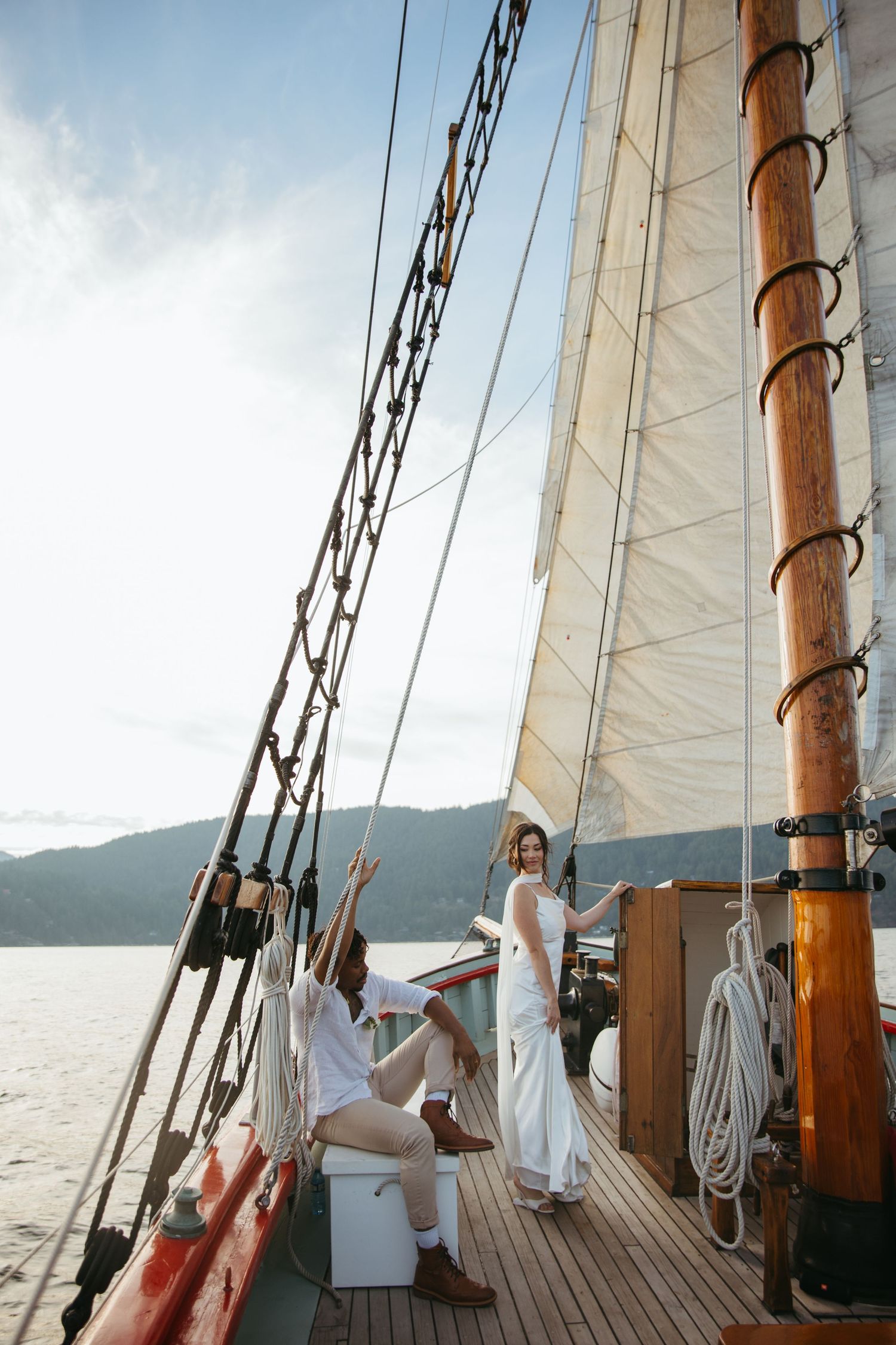 Bride and groom celebrating on deck of classic wooden sailboat on mountain lake.