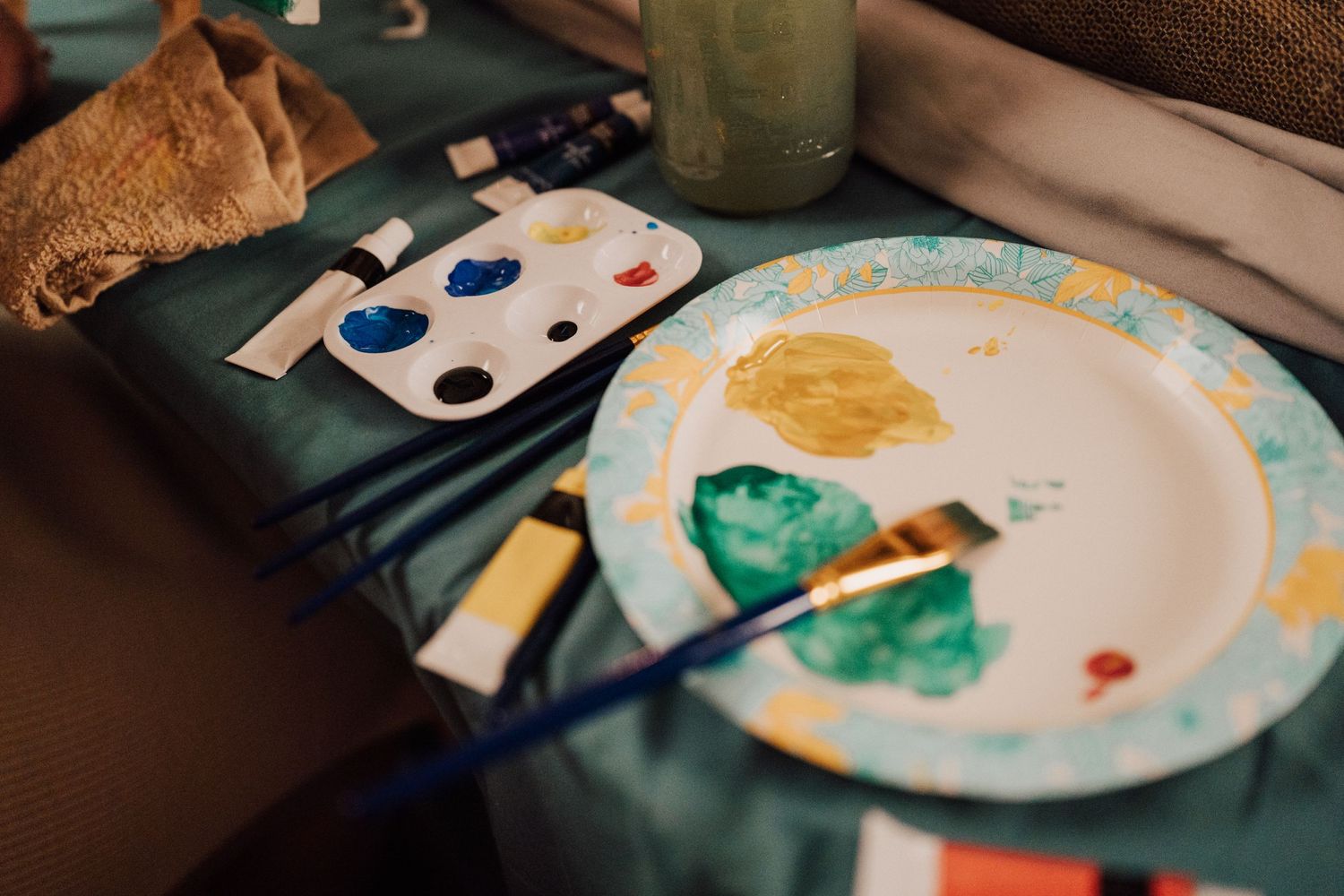 Paint supplies and a plate with artwork sit on a blue surface during a creative session.