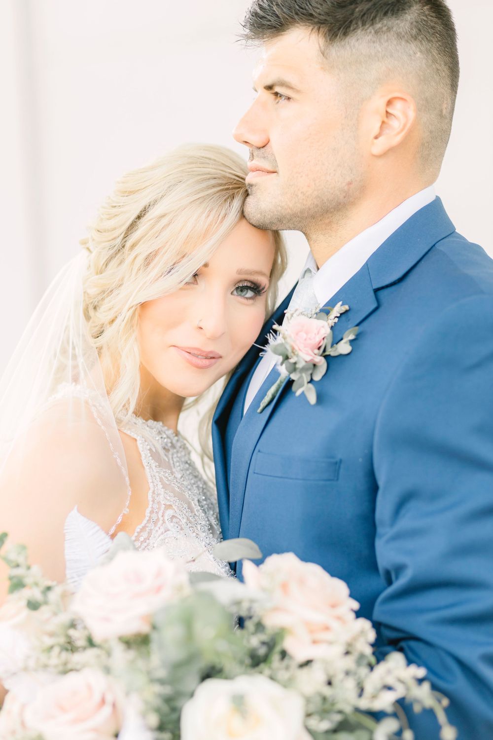 A wedding couple poses together with soft pink floral arrangements.