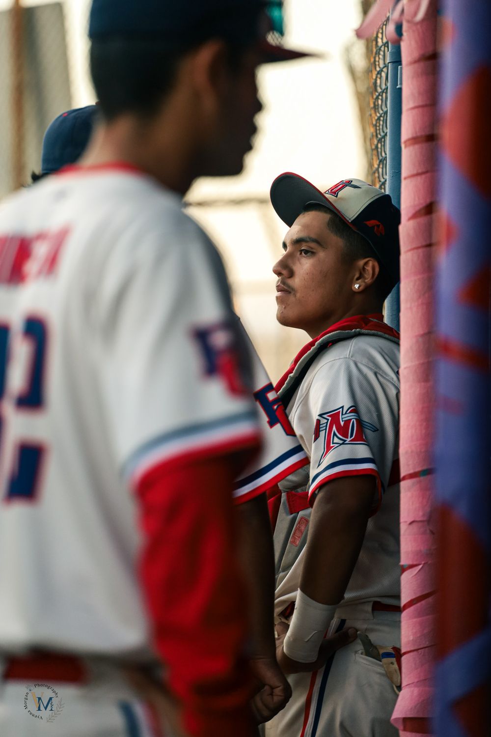 Baseball players in white and red uniforms lined up in dugout during game.