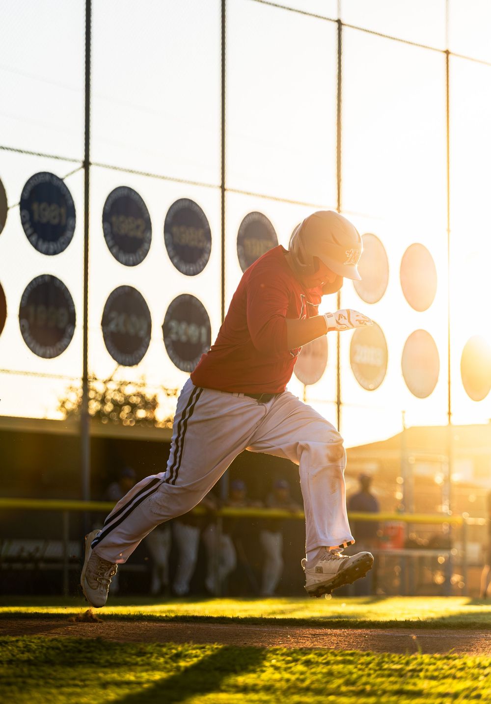 Baseball player leaping to catch a ball during sunset with stadium lights and green field in the background.