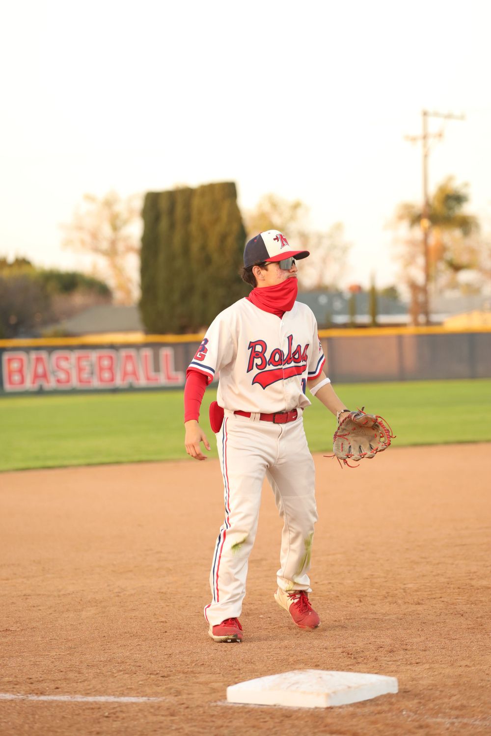 Baseball infielders in white uniforms positioned on the dirt diamond at sunset.