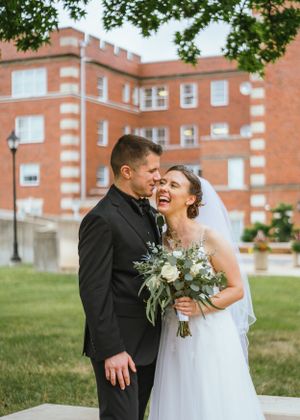 A joyful wedding couple shares a candid moment together on their special day in front of a brick building.