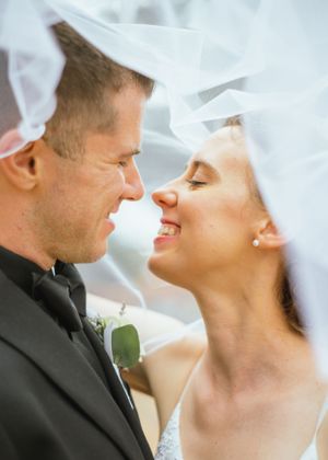 A romantic wedding portrait of a couple under flowing white veil sharing an intimate close moment together.