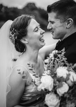 A joyful black and white wedding moment captured showing the bride laughing with her bouquet of roses.