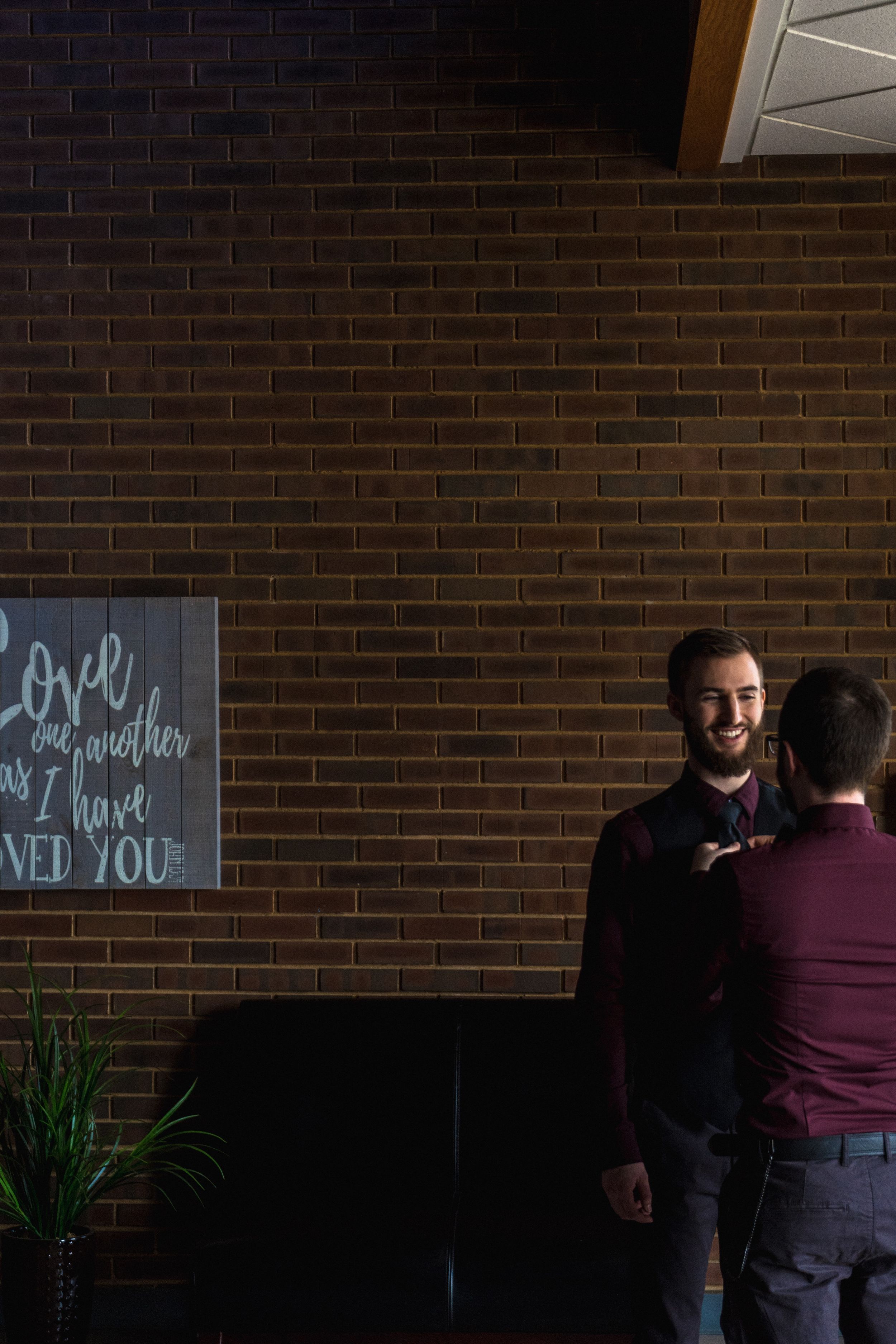 Two people having a conversation in front of a brick wall with an inspirational quote sign in a dimly lit space.
