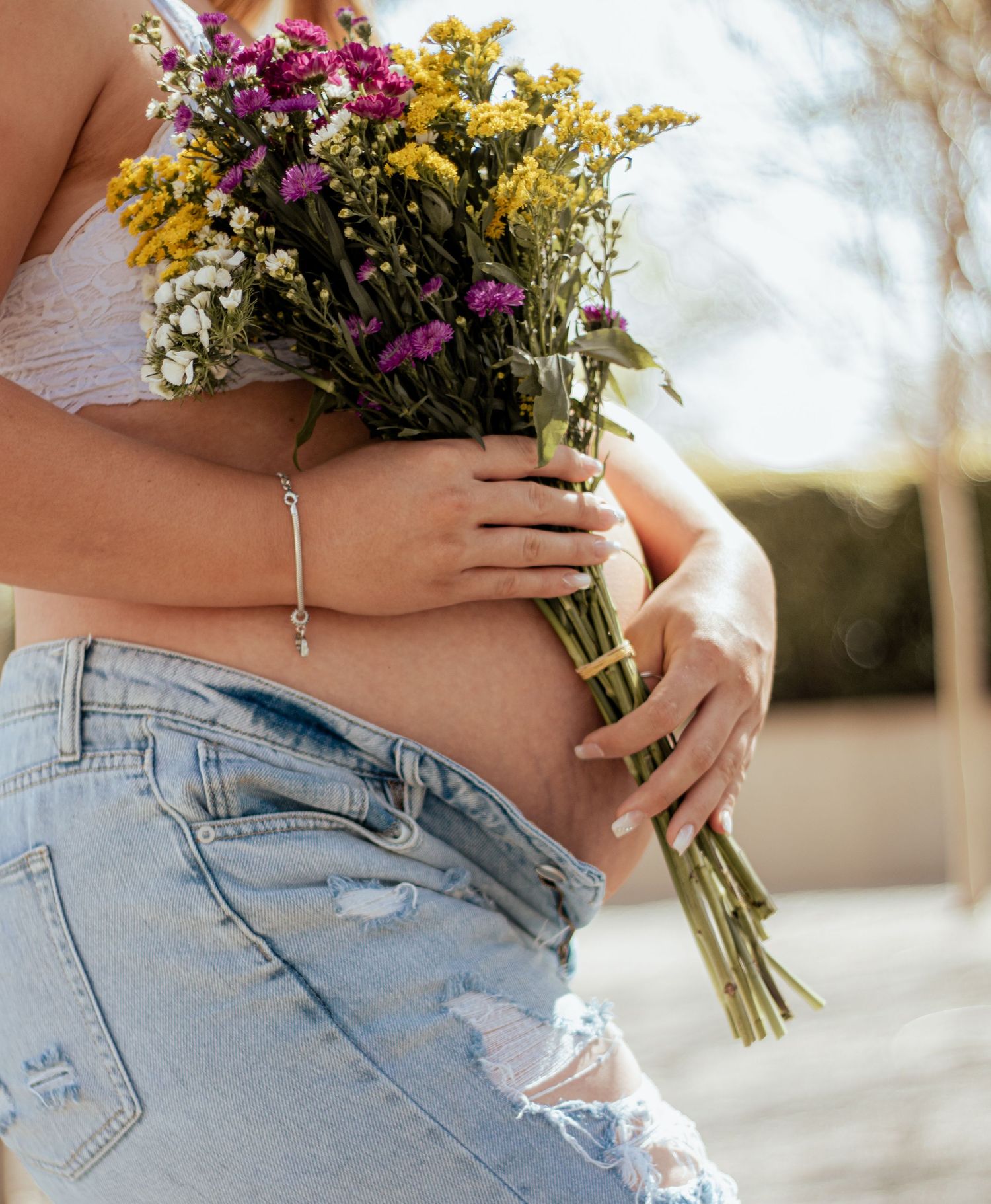 Close-up of hands holding a colorful wildflower bouquet with yellow goldenrod and purple flowers against distressed jeans.