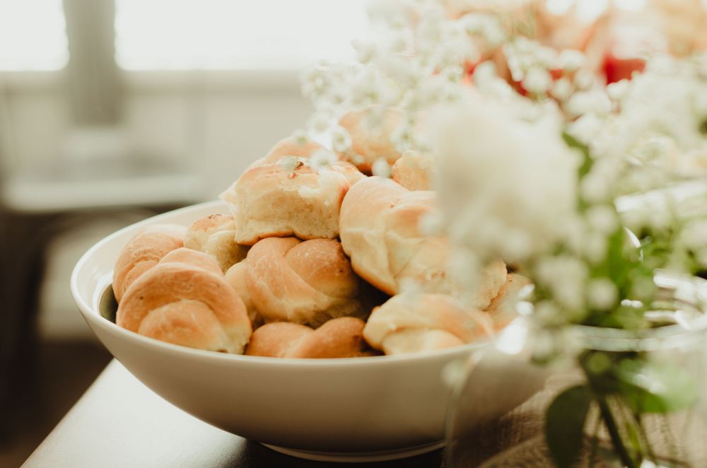 Fresh dinner rolls served in a white ceramic bowl alongside floral decorations and table settings.