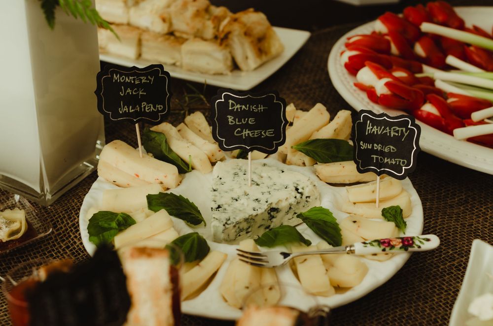 Cheese and appetizer platters with small black label signs displayed at an elegant party spread.