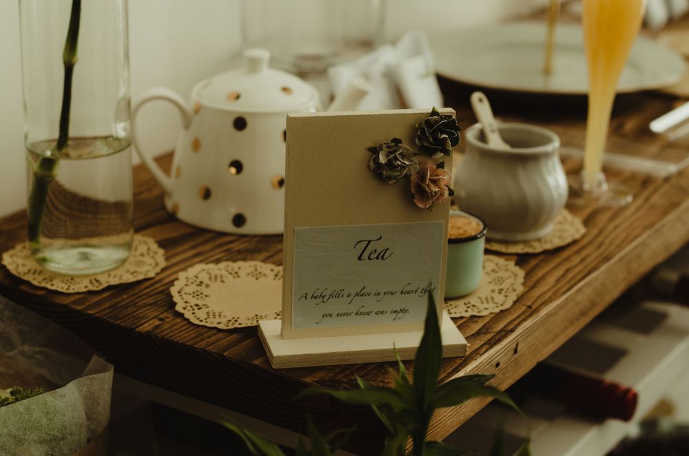A cozy tea setup on a wooden table with a white polka dot teapot, creamer, and vintage inspired menu card.