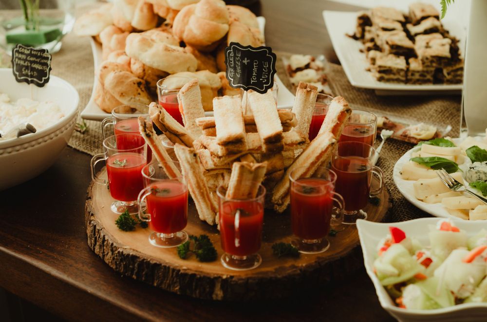 Wooden platter with appetizers including cheese sticks and small red cocktail glasses on a rustic table setting.