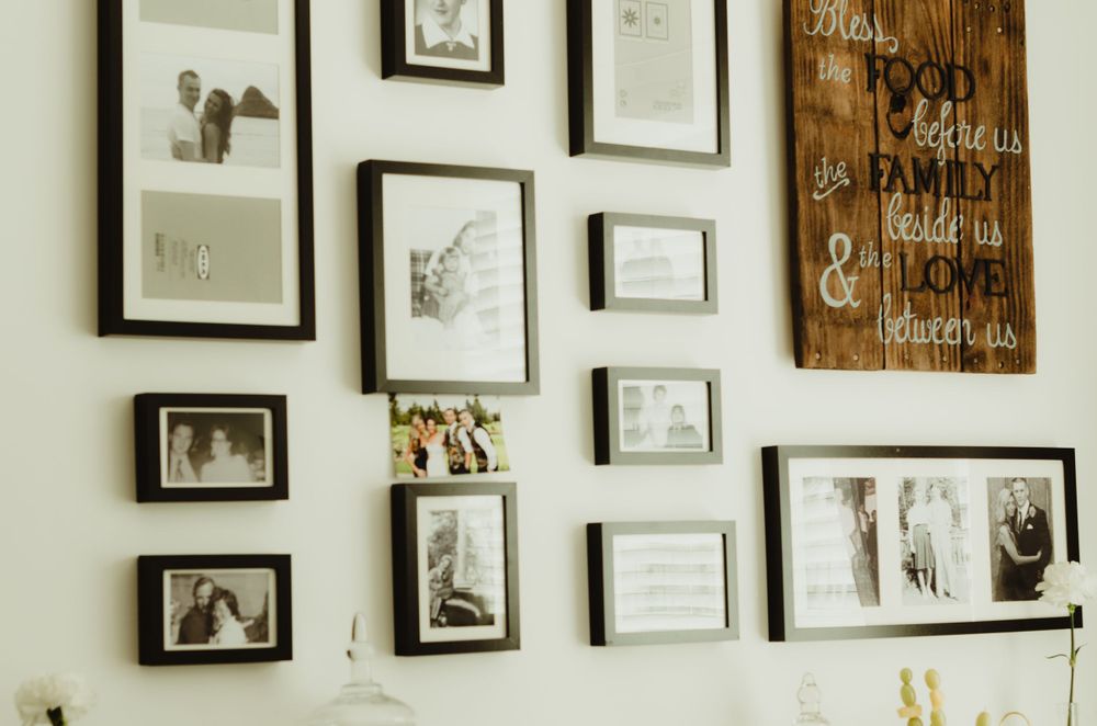 A gallery wall featuring black and white framed photographs and artwork alongside a rustic wooden sign.